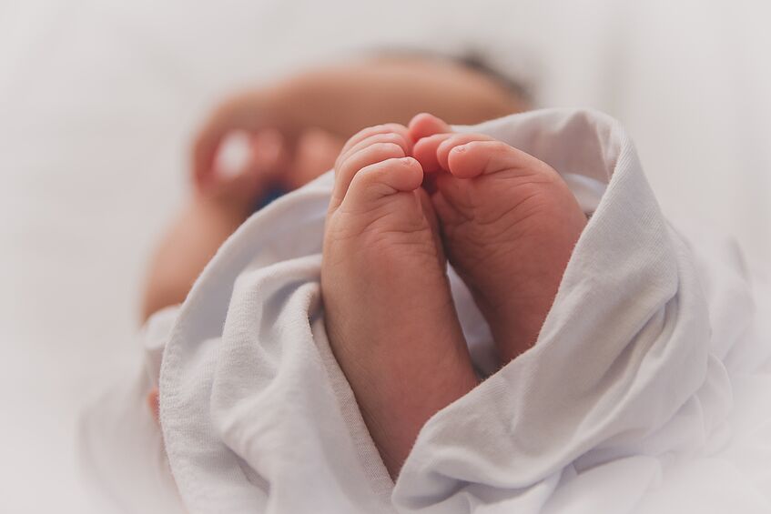 The picture shows a swaddled baby. The tiny feet and the blurred hands can be seen.