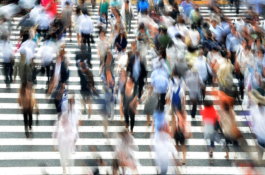 The picture shows a blurred image of many people crossing a street.